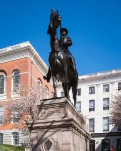Joseph Hooker equestrian statue on a tall stone pedestal with HOOKER inscribed on the base, set against buildings and blooming trees.