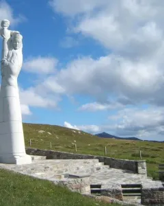 Our Lady of the Isles statue on a tiered stone platform in a grassy landscape with hills behind it