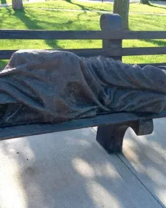 Homeless Jesus bronze sculpture of a sleeping figure on a park bench, with wounded feet exposed at one end.