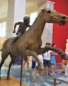 Jockey of Artemision bronze sculpture showing a young rider leaning forward on a horse in motion inside a museum.