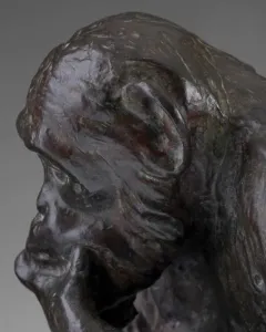 Bronze sculpture of a chimpanzee holding a human skull while seated on books, including one labeled Darwin.