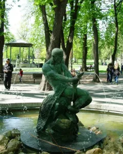 Fisherman Fountain bronze statue of a man wrestling a serpentine creature in a park with trees and paths.