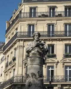Gavarni Fountain with a stone bust of a bearded man writing in a book atop a carved cylindrical pillar.