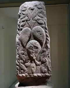 Pfalzfeld Obelisk with carved foliage patterns and three human faces on a stone column.