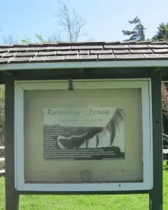 Informational kiosk for Running Fence stands on a grassy lawn near a split-rail fence.