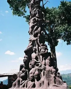 Pillar of Shame sculpture with writhing human figures on a tall dark pillar and plaque at the base.