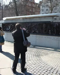 The Battle of Britain Monument with a silver sculpture above dark relief panels and carved stone text, with people standing nearby.