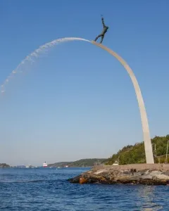God our Father on the Rainbow sculpture with water arcing into the bay beside a rocky shoreline