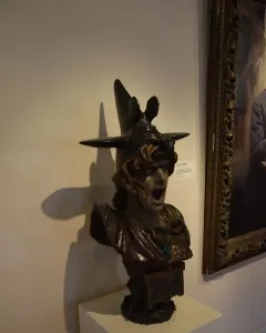 Bellona bust with a winged helmet and open mouth displayed on a white pedestal.