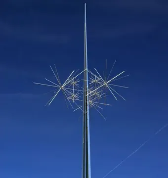 Ad Astra sculpture with a tall metallic pole and white starburst rods against a blue sky.