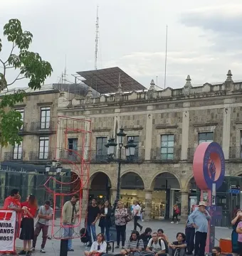 Crowd gathered in a plaza beside the Antimonumento 5J, with banners on the ground in front of an ornate stone building.
