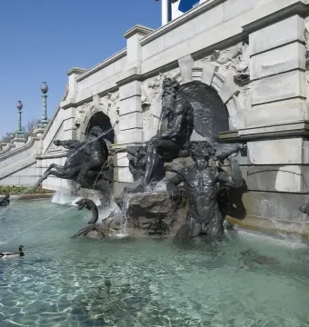 Court of Neptune Fountain with sculpted figures and a duck swimming in the shallow pool