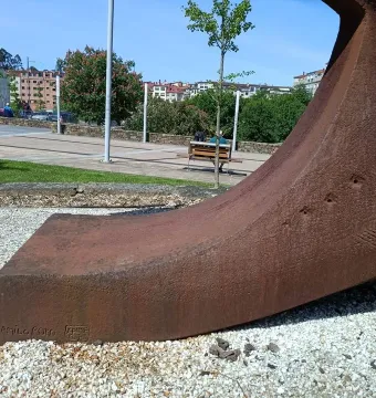 Dorna sculpture with a rust-colored textured curved form resting on white pebbles in a city square.