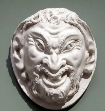 White circular relief sculpture of the Head of a Faun with a grinning face, pointed ears, and curly beard and hair.