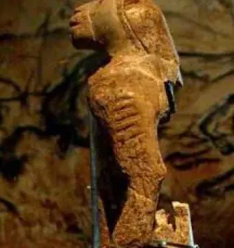 Lion-man figurine with a lion-like head facing left, shown against a dark blurred background.