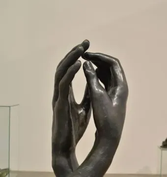 The Cathedral sculpture showing two dark metal hands rising upright with fingertips nearly touching.
