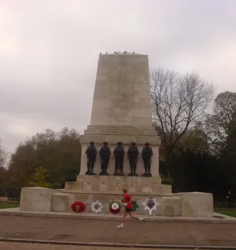 Guards Memorial with five dark soldier statues, floral wreaths at the base, and a runner in red passing by.