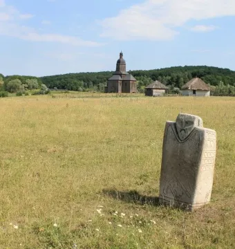 Kernosivka Idol stone monument standing in a grassy field with a church and trees in the background.