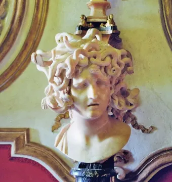 Marble bust of Medusa with coiled snakes for hair and a pained expression, displayed on a pedestal.