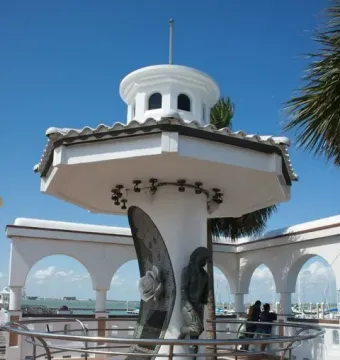 Mirador de la Flor monument with Selena Quintanilla statue, tribute plaque, and rose beside a bay railing.