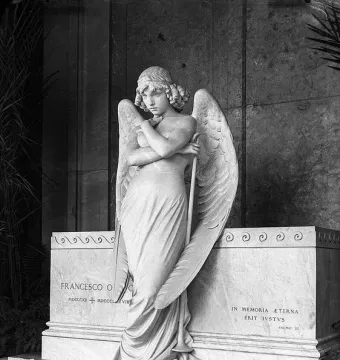 Monteverde Angel marble sculpture standing before the Oneto tomb with wings spread and head bowed.