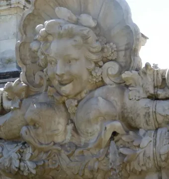 Ornate stone fountain from the Monument aux Girondins with a smiling female face, shell motifs, and sea creatures spouting water.