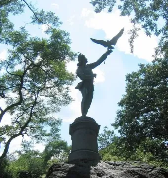 The Falconer statue silhouetted against a bright sky in Central Park, with trees behind it.