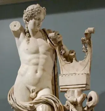 Apollo of Cyrene marble statue with a missing left arm, draped lower body, and a lyre-topped support beside him.