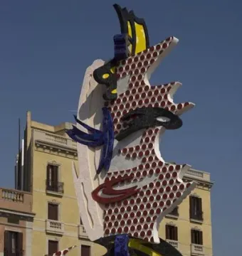 The Face of Barcelona sculpture with red dots, yellow-and-black stripes, and blue mosaic tiling against a blue sky.