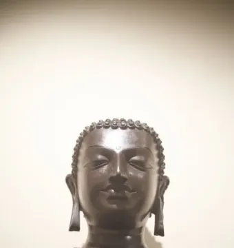 Head and shoulders of the Sultanganj Buddha with curly hair, downcast eyes, and elongated earlobes