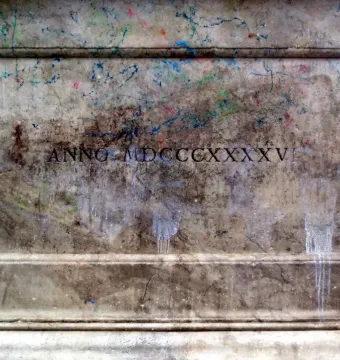 Weathered stone plaque from the Canapone monument with Roman numerals and paint splatters.