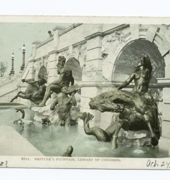 Court of Neptune Fountain with dark metallic statues rising from a pool beside stone arches and steps.