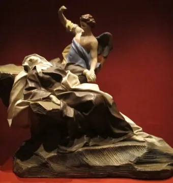 Terracotta sculpture of the Ecstasy of Saint Teresa showing a reclining robed figure and a winged angel above against a red background.