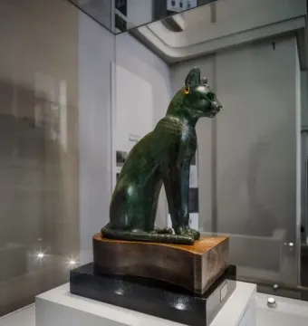 The Gayer-Anderson cat, a bronze cat statue with gold earrings, a nose ring, and an etched collar, displayed in a glass case.