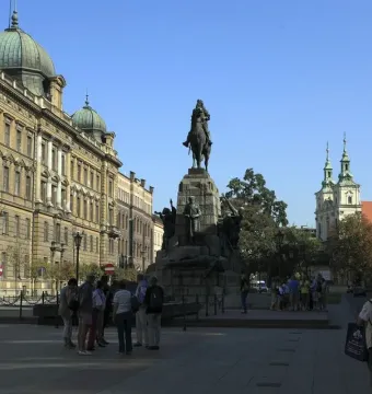 Grunwald Monument with an equestrian statue on a stone pedestal in a city square, with historic buildings and people nearby.