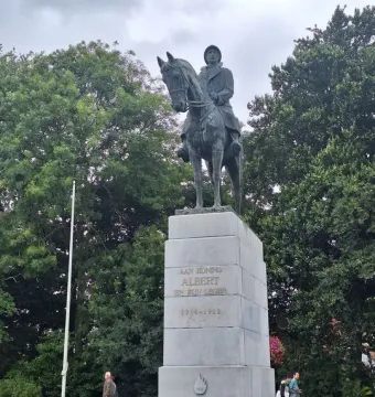 Bronze equestrian statue of King Albert I on a stone pedestal in a park, with trees and a few people in the background.