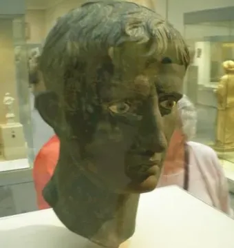 Meroë Head bronze sculpture with short curly hair and prominent eyes on a pedestal