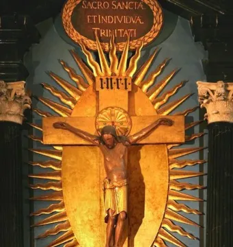 Gero Cross with a dark carved Christ figure on a golden crucifix, framed by Latin inscriptions and a sunburst backdrop.
