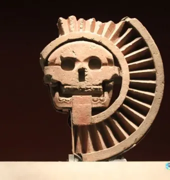 Disk of Mictlāntēcutli showing a skull-like face with hollow eyes and teeth, framed by a ridged semicircular form.