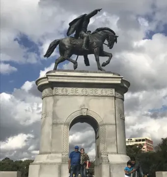 Sam Houston statue of a man on horseback atop a tall stone archway with people on the steps below.