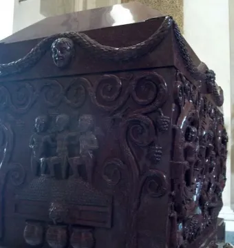 Sarcophagus of Constantina with carved reliefs of figures, garlands, and grapevines on a dark red stone surface.