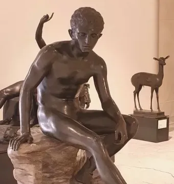 Seated Hermes bronze statue of a nude young man on a rock, looking downward with a winged sandal visible.