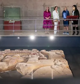 Tlaltecuhtli Monolith displayed on a dark platform with visitors observing from an elevated walkway.
