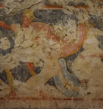 Weathered painted fragment from the Amazon Sarcophagus showing faded figures in red, orange, white, and blue.