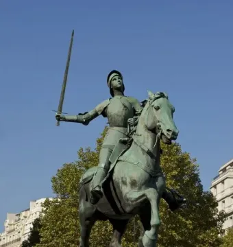 Joan of Arc equestrian statue in medieval armor holding a raised sword on a stone pedestal in Paris.
