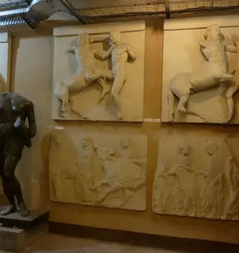Parthenon metope relief panels showing damaged mythological battle scenes, with a dark headless statue in the foreground.
