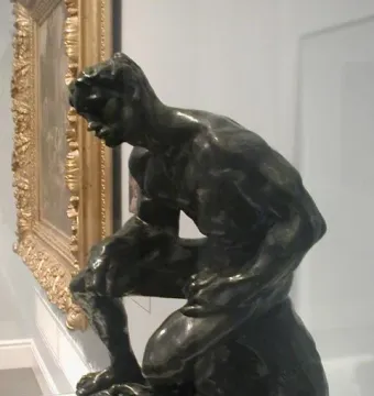 Rodin\'s The Athlete shown in three-quarter view on a green marble pedestal.
