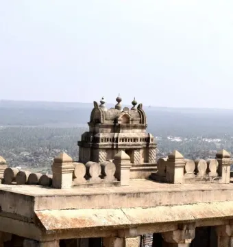 A multi-tiered stone shrine overlooking a hazy green landscape under a clear sky.
