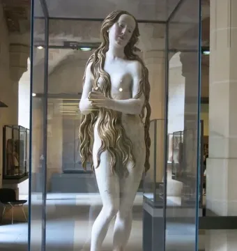 Mary Magdalene sculpture of a standing female figure with long wavy hair, displayed in a glass case.