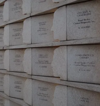 The Postcards memorial shows rows of engraved name plaques on a light stone wall, each with a carved human silhouette along the edge.